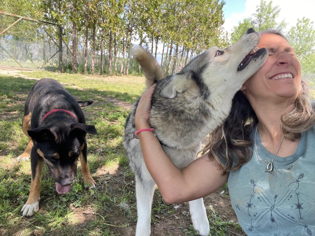 Vanesa riéndose mientras un perro tipo lobo le lame la cara en la finca